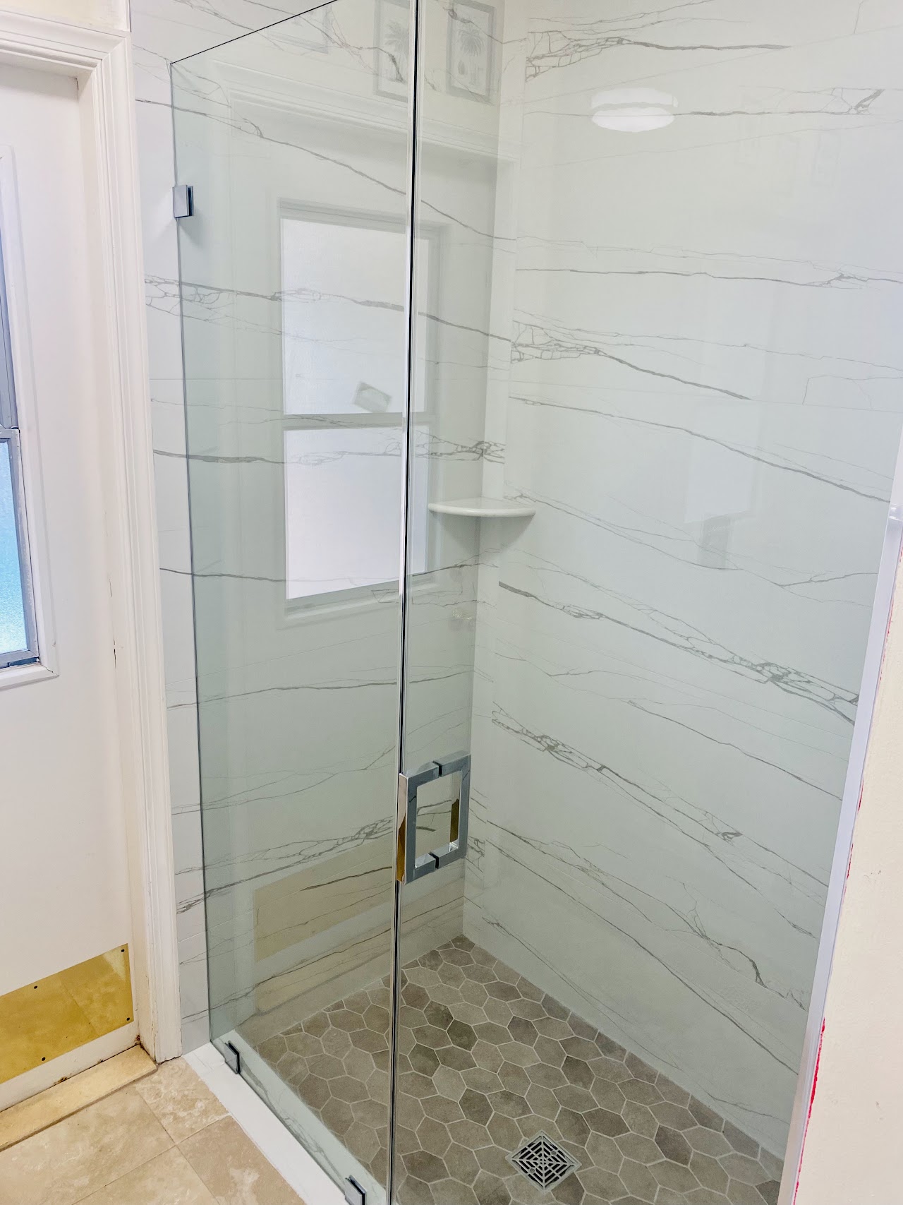 Glass shower door in white tile bathroom